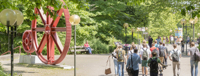 Students in summer on north campus, red gears in background.