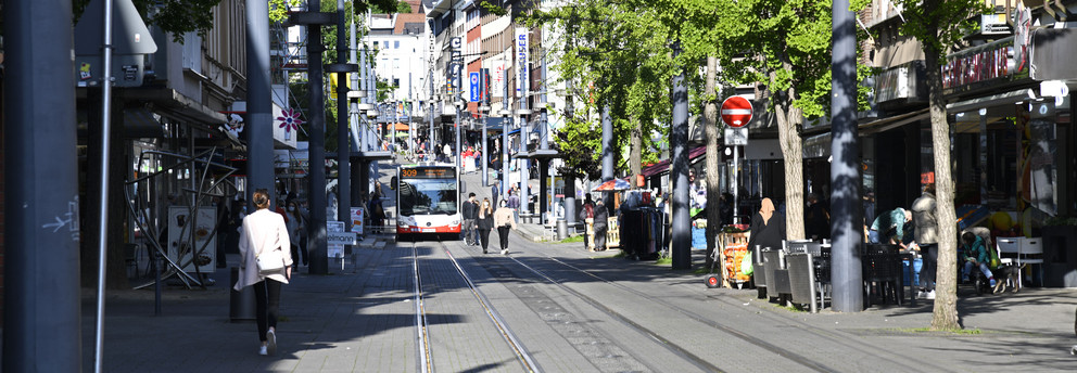 A pedestrian area in the german city Witten. A bus driving and people strolling in the area are depicted.  