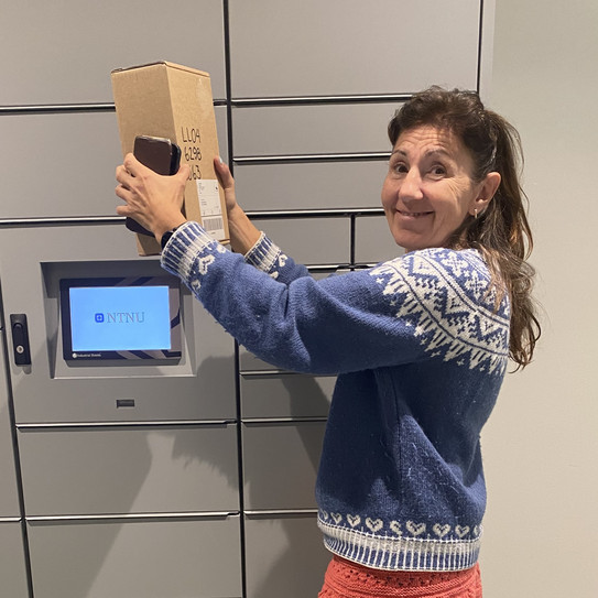 Trude Tørset in front of a pick-up station holding a parcel in her hands